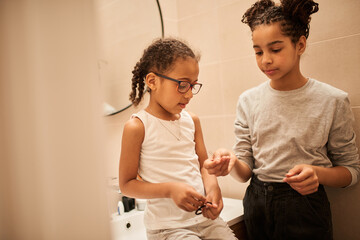 Girl wearing glasses sitting at the bathroom and waiting while her sister making braids
