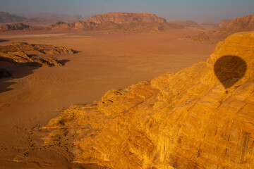 The view of Wadi Rum desert from a hot air balloon at sunrise, with the shadow of that balloon seen...