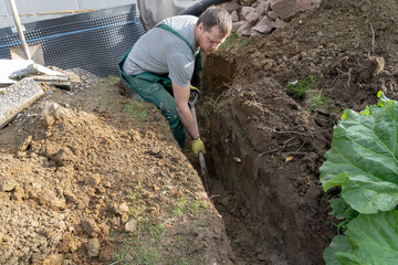 A man is digging a ditch in his garden with a shovel.