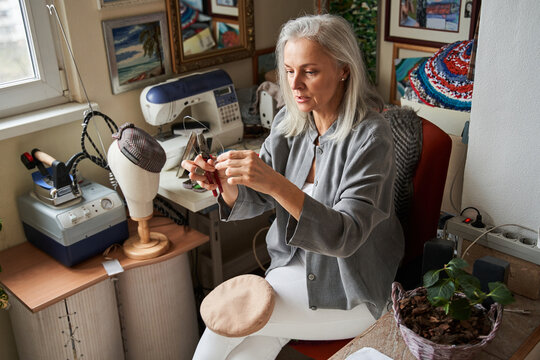 Female hats maker shape the hat in her workshop, while holding forceps and carcass - Powered by Adobe