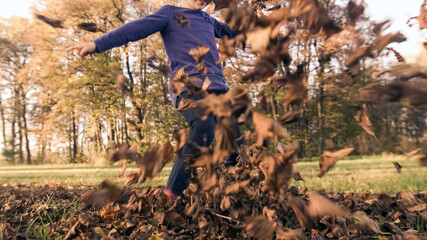 Ground angle shot of a caucasian preschool girl hitting, like a ball, heap of dry leaves into a camera, byciklist in the background