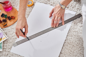 Woman sitting at the floor and outlines with a pencil and ruler some shapes