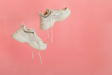 White sneakers flying. Female white leather shoes with laces on pink background. Pair of stylish sneakers Comfortable sportswear hipster womens shoes. Copy space.