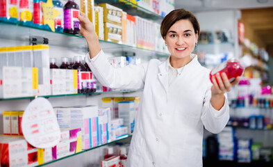Fototapeta na wymiar Young friendly smiling female pharmacist suggesting useful body care products in pharmacy