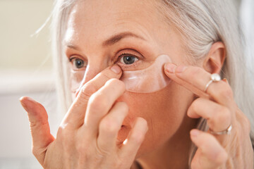 Female is looking into the mirror while wearing eye patches against wrinkles