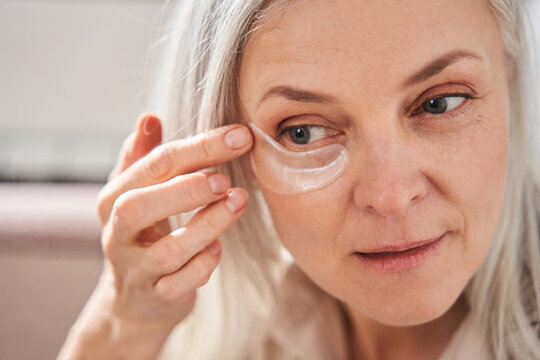 Grey haired woman putting patches at the face at the morning