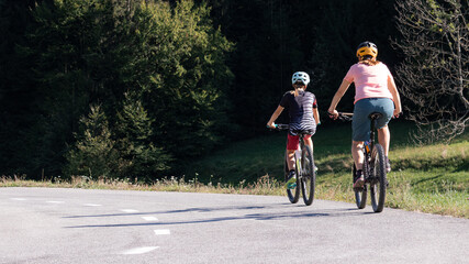 Woman and girl child riding mountain bikes on a country road in nature on a bright sunny summer day.