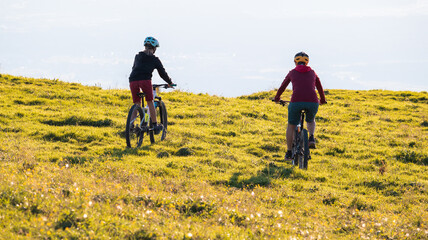 Mother and daughter cycling downhill with mountain bikes at a sunset.