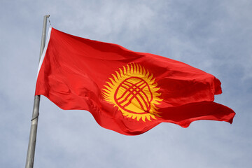 Kyrgyzstan flag waving at a pole in Bishkek. Red flag with yellow tunduk in front of sky.