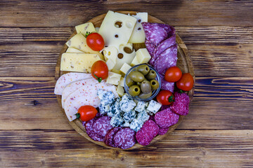 Slices of various types of cheese and dry smoked salami sausage on wooden background. Traditional italian antipasto platter. Top view