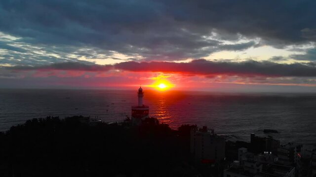 Lighthouse at sunrise of east coast sea of Korea. Sun is glowing red and  gold and clouds are turning reddish. Beautiful nature and landmark aerial drone footage took with 4K 30fps.