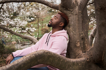 Man leaning on the tree with closed eyes and resting at the nature