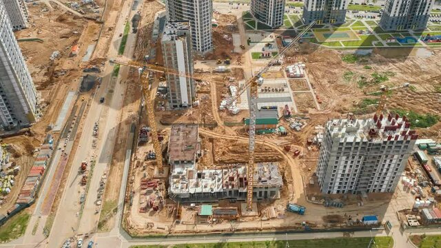 Aerial time-lapse hyperlapse tower cranes working on construction site in city. Drone shot constructions development on sunny day. Machinery and workers employed. Builders work on residential building