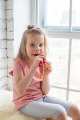 Portrait of preschool-aged caucasian girl puts on the lips hygienic lipstick