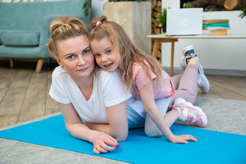 Portrait of mother with daughter in sportswear lying on a yoga mat