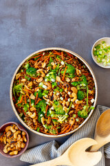 Grain salad with carrot, broccoli, cashew nuts, with napkins, on a gray surface