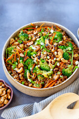 Grain salad with carrot, broccoli, cashew nuts, with napkins, on a gray surface