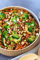 Grain salad with carrot, broccoli, cashew nuts, with napkins, on a gray surface