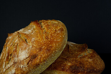 Two round artisan loaves of freshly baked specialty sourdough bread sit cooling in front of a black background.