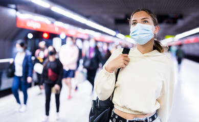 Portrait of an active girl in a protective mask, walking on a subway platform during a pandemic, with a backpack..on her bask