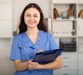 Positive woman doctor in formal wear standing with folder in office