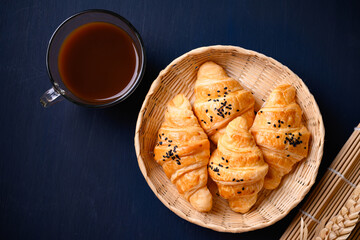 French croissant with black sesame seeds and coffee cup on black background, morning breakfast, Top view