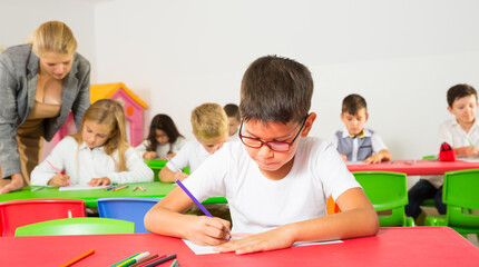 Portrait of boy student of primary school doing his task at desk in classroom