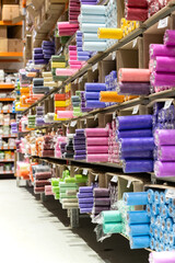 Fabric store interior with rolls of textile on racks. Colorful clothes for sale in warehouse stock. Empty tailoring shop with big assortment of material on shelves for design, sewing and dressmaking