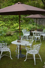 A white outdoor patio set with umbrella with white chairs and tables on green grass.