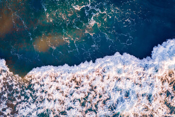 Foamy wave of clear turquoise ocean water near the sandy shore, Aerial top view