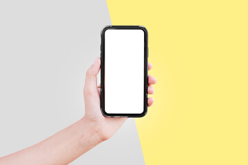 Close-up of male hand holding smartphone with mockup on yellow and grey backgrounds. Colors of the year 2021; ultimate gray and illuminating.