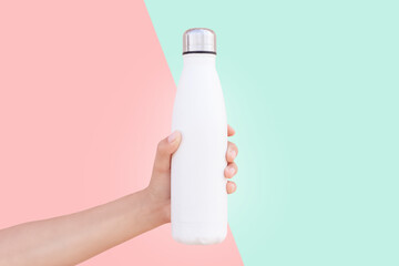 Close-up of female hand holding white reusable steel thermo water bottle isolated on two background...