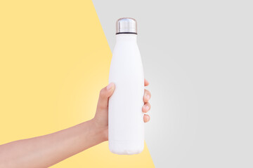 Close-up of female hand holding white reusable steel thermo water bottle isolated on two...