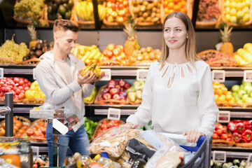 Portrait of happy positive smiling woman satisfied with purchases in shopping cart at fruit store