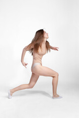 Fototapeta premium Young slender girl, with long hair, in a beige bodysuit, dancing in the white studio. motion blur