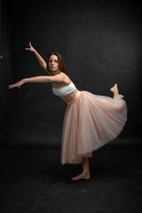 Young girl in white top and peach skirt dancing in black studio