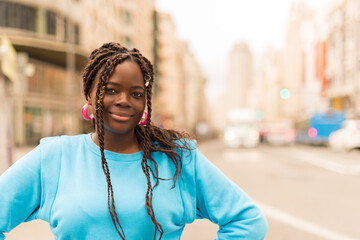 Pretty young black woman in the middle of the city, smiling at camera.