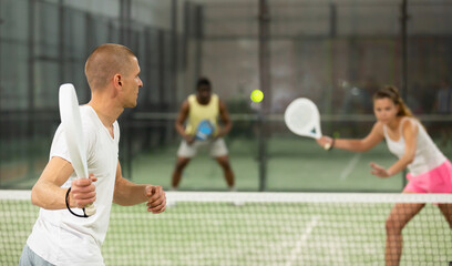 Concentrated man padel player hitting ball with a racket on a hard court