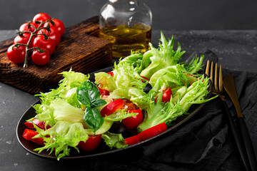  Simple summer salad of lettuce, tomatoes with olives and olive oil on a black plate close-up