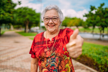 Joyful senior lady in glasses laughing up thumb. Latin American woman. Brazilian elderly woman. - obrazy, fototapety, plakaty