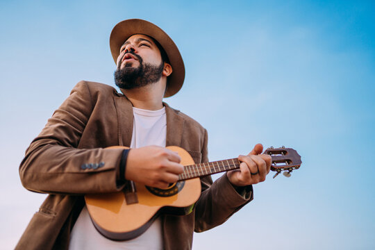 Outdoor of a young Latin American man playing cavaquinho or ukulele. Brazilian musician.