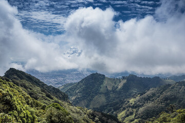 Line of mountains with grass and trees surrounding the capital of Costa Rica on a sunny day full of white clouds