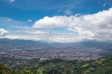 panoramic view of the green and tree-filled mountains surrounding the capital of San Jose, Costa Rica on a sunny morning with white clouds