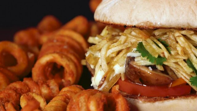 hamburguer with small chips and mushrooms and curly fries rotating on wooden base from left to right