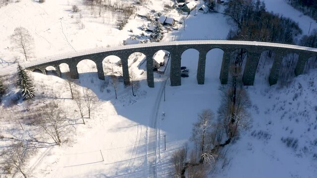 Stone train railroad viaduct towering above a small village,snowy.