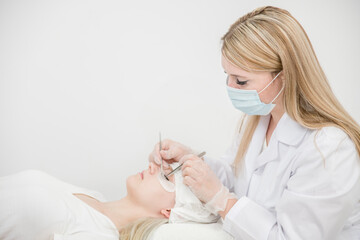Fototapeta na wymiar Cosmetologist wearing protective face mask lengthening female lashes in beauty salon