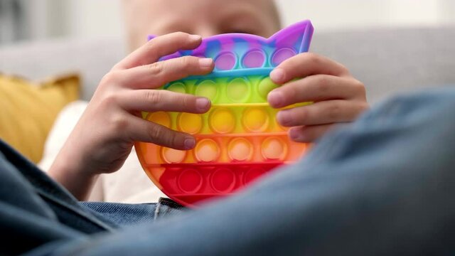 Child play with pop it sensory toy. Boy presses on colorful rainbow squishy soft silicone bubbles. Stress and anxiety relief. Trendy fidgeting game for stressed children and adults