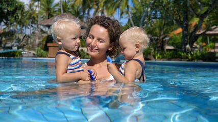 Fototapeta na wymiar Activities ideas for travelling with kids. Mother of twin girls spending time in a swimming pool with them