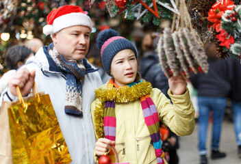 Cheerful preteen girl with father shopping decorations on Christmas market..