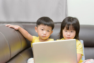 Little Asian boy and girl learning or gameing on laptops together  at home